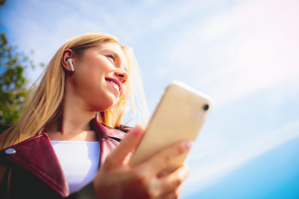 woman with ear buds holding phone and smiling